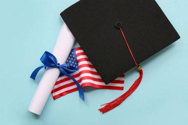 Mavi kurdeleli diploma, Amerikan bayrağı ve açık mavi arka planda mezuniyet şapkası.