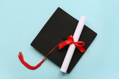 Kırmızı kurdeleli diploma ve açık mavi arka planda mezuniyet şapkası.