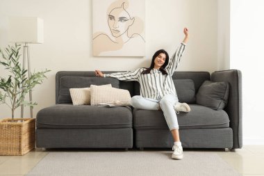 Oturma odasındaki siyah kanepede dinlenen genç kadın.