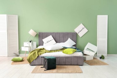 İçinde posterler ve ters çevrilmiş puf olan dağınık bir yatak odası.