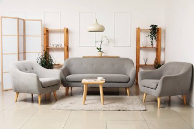 Gri kanepeli, koltuklu ve beyaz duvarın yanındaki katlanmış ekranlı oturma odasının içi.