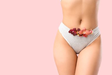 Pembe arka planda güzel orkide çiçekleri olan külotlu genç bir kadın.