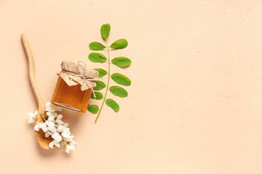 Akasya çiçekli tatlı bal kavanozu ve bej arka planda ahşap kaşık.