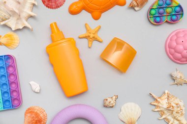 Gri arka plandaki çocuklar için güneş kremi ve plaj aksesuarlarıyla güzel bir kompozisyon