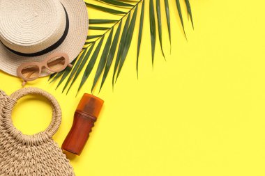 Sarı arka planda plaj çantası, güneş gözlüğü, şapka ve güneş kremi ile güzel bir kompozisyon.