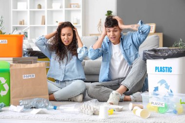 Stresli genç bir çift, ellerinde çöp konteynırlarıyla evdeki çöpleri düzenliyorlar. Geri dönüşüm kavramı