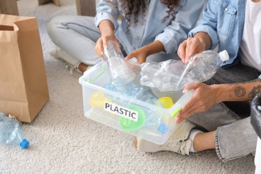 Genç bir çift evdeki çöp kutusuna plastik çöp atıyor. Atık sıralama kavramı