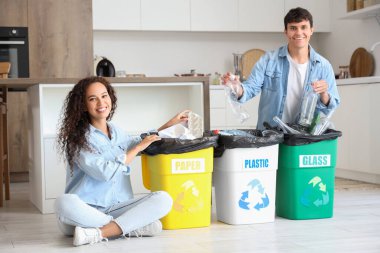 Mutfaktaki çöpleri düzenleyen çöp konteynırları olan genç bir çift. Geri dönüşüm kavramı
