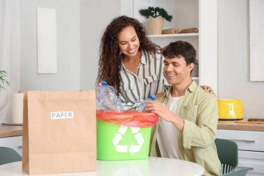 Genç bir çift mutfaktaki çöp konteynırına plastik şişe atıyor. Geri dönüşüm kavramı