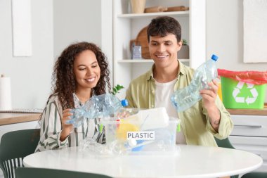 Genç bir çift mutfaktaki çöp konteynırına plastik şişe atıyor. Atık sıralama kavramı