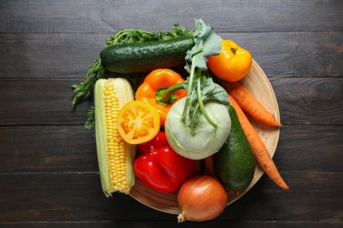 Siyah ahşap arka planda farklı taze sebzeli tabak.