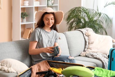 Evdeki kanepede giysilerini bavula koyan genç bir kadın. Yaz yolculuğu konsepti