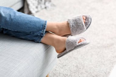 Oturma odasındaki kanepede yumuşak terlikler içinde kadın bacakları.