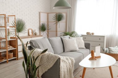 Oturma odasının içinde kanepe, katlanan perde ve bitkiler var.