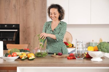 Olgun bir kadın mutfakta sebze salatası pişiriyor.