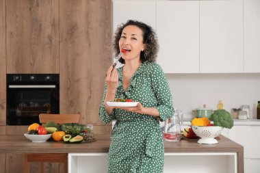 Mutfakta sebze salatası yiyen olgun bir kadın.