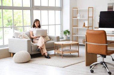 Genç iç mimar koltukta dizüstü bilgisayarla çalışıyor.