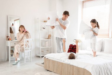 Mutlu ebeveynler ve küçük çocukları yatak odasında yastık kavgası yapıyor.