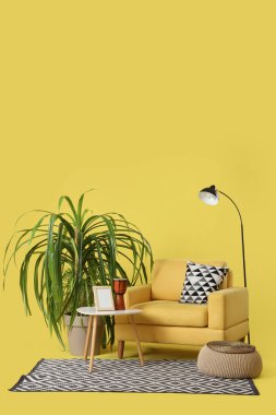 Sarı arka planda lamba, masa ve palmiye ağaçları olan koltuk.