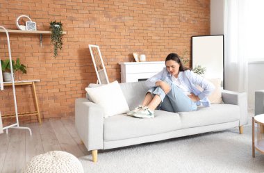 Evdeki koltukta regl sancısı çeken genç bir kadın.