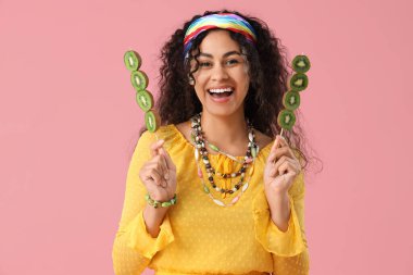 Güzel, genç, mutlu, Afro-Amerikalı bir kadın pembe arka planda kivi çubukları tutuyor.