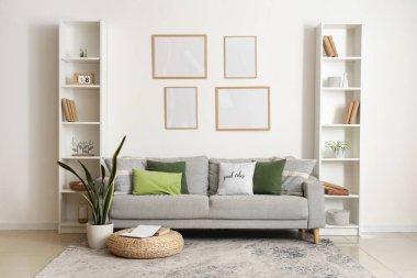 Yastıklı rahat kanepe, çiçek, kitap ve çerçeveli puf oturma odasında.