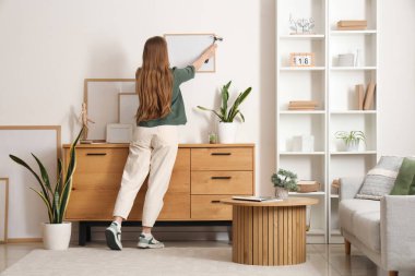 Oturma odasındaki duvara çerçeveyi asan genç bir kadın.