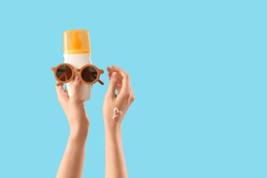 Kalp kremi ve güneş kreminden yapılmış, mavi arka planda güneş gözlüğü olan kadın elleri.