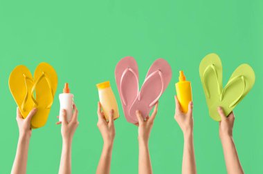 Yeşil arka planda parmak arası terlikleri ve güneş kremleri olan kadın elleri.