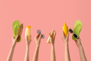 Plaj aksesuarları ve pembe arka planda güneş kremleri olan kadın elleri.