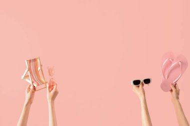 Parmak arası terlik, mini iskemle ve pembe arka planda güneş gözlüğü takan kadın eller.