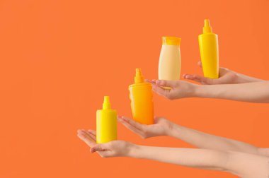 Turuncu arka planda güneş kremi şişeleri olan kadın elleri.