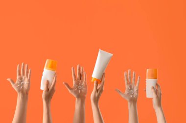 Güneş kremadan yapılmış kadın elleri ve turuncu arka planda güneş kremi şişeleri.