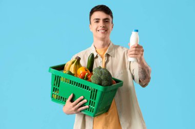 Mavi arka planda alışveriş sepeti olan genç bir adam.