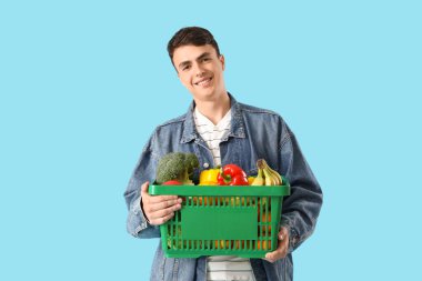 Mavi arka planda alışveriş sepeti olan genç bir adam.