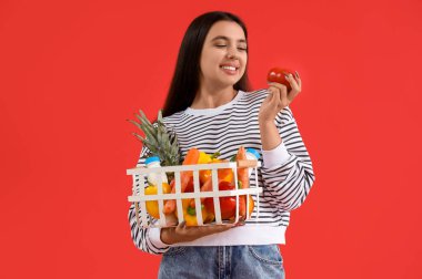 Kırmızı arka planda domatesli ve alışveriş sepetli genç bir kadın.