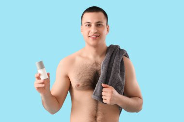 Deodorantı ve mavi arka planda havlusu olan yakışıklı bir genç.
