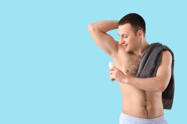 Yakışıklı genç adam mavi arka plana deodorant sürüyor.