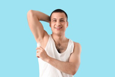 Yakışıklı genç adam mavi arka plana deodorant sürüyor.
