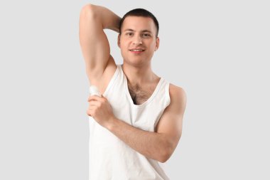 Gri arka plana deodorant süren yakışıklı genç adam.