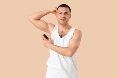 Bej arka plana deodorant süren yakışıklı genç adam.