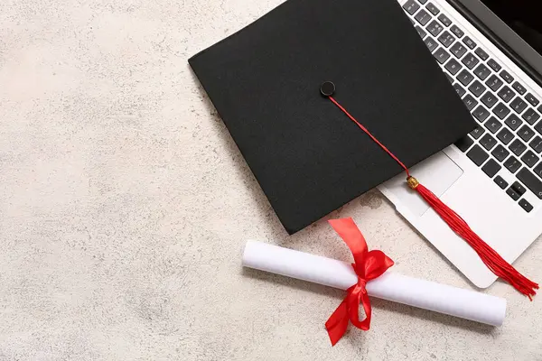 Kırmızı kurdeleli diploma, modern laptop ve beyaz grunge arka planda mezuniyet şapkası.