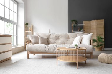 Oturma odasının içinde bej kanepe, masa ve raf üniteleri var.