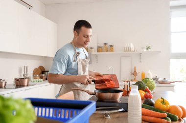 Genç adam mutfakta tavaya dolma biber koyuyor.