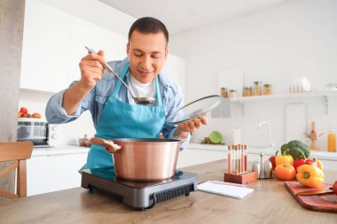 Genç adam mutfakta çorba tadıyor.