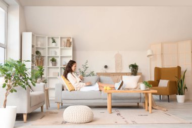 Genç Asyalı kadın evdeki kanepede dizüstü bilgisayar kullanıyor.