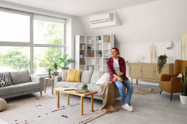 Kulaklıklı genç adam evdeki kanepede oturuyor.