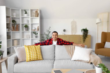 Evdeki gri kanepenin arkasındaki genç adam.