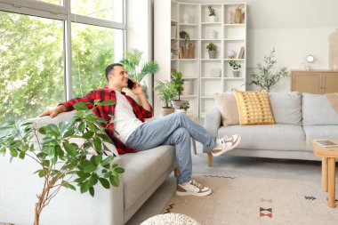 Evde kanepede cep telefonuyla konuşan genç adam