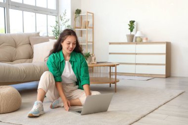 Genç Asyalı kadın evde dizüstü bilgisayar kullanıyor.